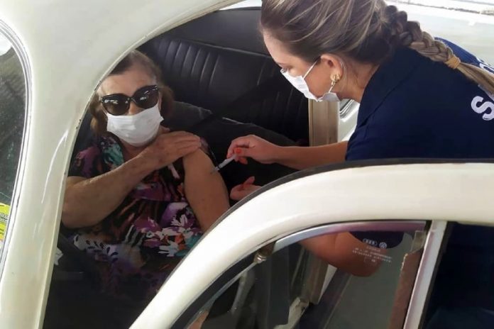 idosa usando máscara e óculos escuro é vacinada por profissional de saúde dentro de um fusca