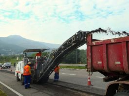 Prefeitura inicia obra na Via Expressa Sul, em Florianópolis maquina recortando asfalto da via expressa sul e jogando detrito em caçamba de caminhão; operários ao lado; trânsito ao fundo