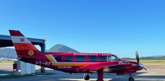 Na foto observa-se um céu azul e um avião arcanjo do corpo de bombeiros parado na pista. O arcanjo é vermelho com detalhes em amarelo e identificação em branco. O veículo fará a transferência de pacientes de SC para o Espírito Santo.