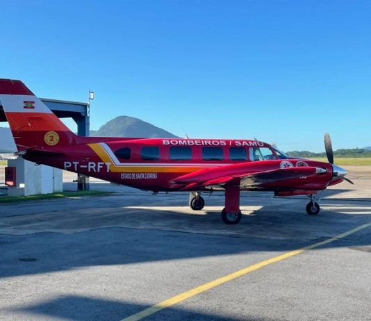 Pacientes de Santa Catarina começam a ser transferidos para o Espírito Santo Na foto observa-se um céu azul e um avião arcanjo do corpo de bombeiros parado na pista. O arcanjo é vermelho com detalhes em amarelo e identificação em branco. O veículo fará a transferência de pacientes de SC para o Espírito Santo.