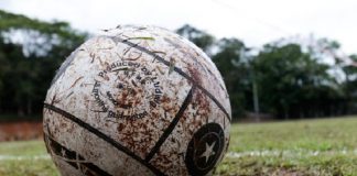 Uma bola branca suja de barro e ao fundo um campo de grama. A foto ilustra a alteração do governo no decreto de medidas restritivas, agora os esportes recreativos estão autorizados em SC.