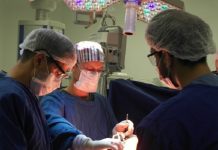 Três profissionais da saúde com roupas azuis, máscaras e proteção nos olhos e cabelos se concentram em um procedimento cirúrgico. As cirurgias eletivas em Santa Catarina estão suspensas na rede privada até o fim de março.