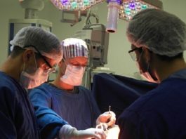Hospital Regional de São José realiza mutirão de cirurgias de mão Três profissionais da saúde com roupas azuis, máscaras e proteção nos olhos e cabelos se concentram em um procedimento cirúrgico. As cirurgias eletivas em Santa Catarina estão suspensas na rede privada até o fim de março.