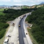 foto aérea de trecho da rodovia perto de mata e máquinas na pista parcial de asfalto - Contorno Viário: consórcio busca mão de obra local