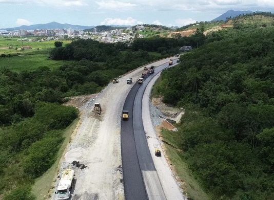 Contorno viário: consórcio busca mão de obra local foto aérea de trecho da rodovia perto de mata e máquinas na pista parcial de asfalto - Contorno Viário: consórcio busca mão de obra local