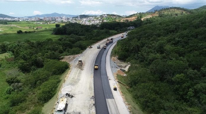 foto aérea de trecho da rodovia perto de mata e máquinas na pista parcial de asfalto - Contorno Viário: consórcio busca mão de obra local
