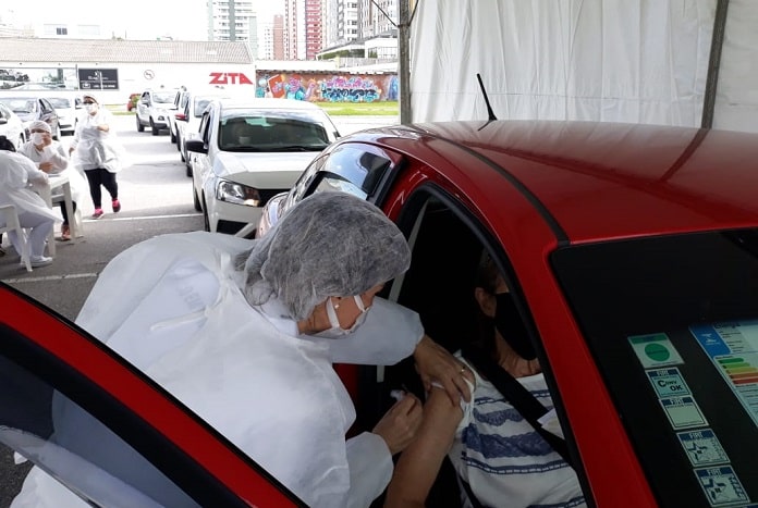 mulher se inclina para vacinar idoso dentro de carro - continua a vacinação contra covid em são josé