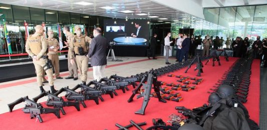 Alesc destina mais de R$ 11 milhões para viaturas e armas da Polícia Militar No tapete vermelho da Alesc os armamaentos estão distribuídos lado a lado. Ao fundo da foto pessoas reunidas e mais a frente um grupo de policiais militares fardados. A Polícia Militar de SC recebeu hoje viaturas e equipamentos em ato simbólico na assembleia.