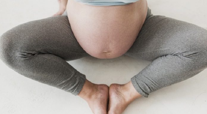 A foto mostra a barriga de uma grávida com calça legging cinza e pernas abertas enquanto os pés se tocam. As doulas de Santa Catarina podem voltar a auxiliar nos partos de hospitais públicos depois de um anos do serviço interrompido.