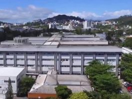 Visão de cima do HU/UFSC. Aprecem algumas árvores e prédios ao fundo. O Hospital tem alguns prédios lado a lado, o que aparece na frente tem cor cinza e branco. Nesta semana, o HU fechou a emergência pediátrica para atender adultos em estado crítico da Covid.