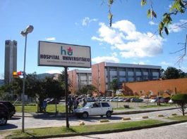 Termina a greve no HU; veja acordo Visão do HU/UFSC onde aparece oe stacionamento com um uno branco parado, há uma placa que sinaliza que ali é o Hospital Universitário da UFSC, ao fundo se vê prédios alaranjados. Nesta semana, o HU fechou a emergência pediátrica para atender adultos em estado crítico da Covid.
