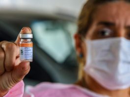 Falta de Coronavac preocupa quem aguarda pela segunda dose; novo lote chega no sábado pessoas usando máscara mostra ampola de vacina - novo lote de vacinas contra a covid-19