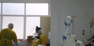 dois profissionais de saúde vistos de costas dentro de hospital; eles usam epi. em primeiro plano paciente intubado - sc tem fila de espera de uti de quase 400 pacientes