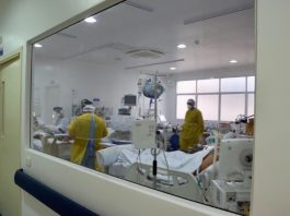 Fila de espera: 380 pessoas aguardam leito de UTI e 81 aguardam por enfermaria profissionais e pacientes dentro de uti vistos através de janela - fila de espera em sc