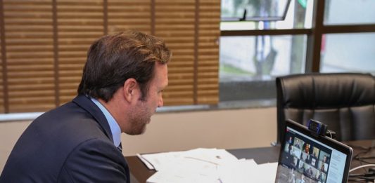 OAB/SC abre canal de denúncias de “fura-fila” da vacina O presidente da OAB/SC de terno escuro em frente ao computador em reunião virtual. Sob a mesa papeis e ao fundo uma janela parte fechada com cortina e parte aberta.