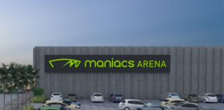 Projeto da arena de esportes de areia que será sediada em Biguaçu. Com um estacionamento e alguns carros, ao fundo se vê a arena identificada com letras verdes "maniacs arenas"