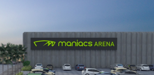 Projeto da arena de esportes de areia que será sediada em Biguaçu. Com um estacionamento e alguns carros, ao fundo se vê a arena identificada com letras verdes "maniacs arenas"