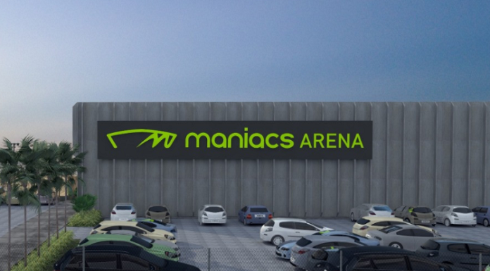 Projeto da arena de esportes de areia que será sediada em Biguaçu. Com um estacionamento e alguns carros, ao fundo se vê a arena identificada com letras verdes "maniacs arenas"