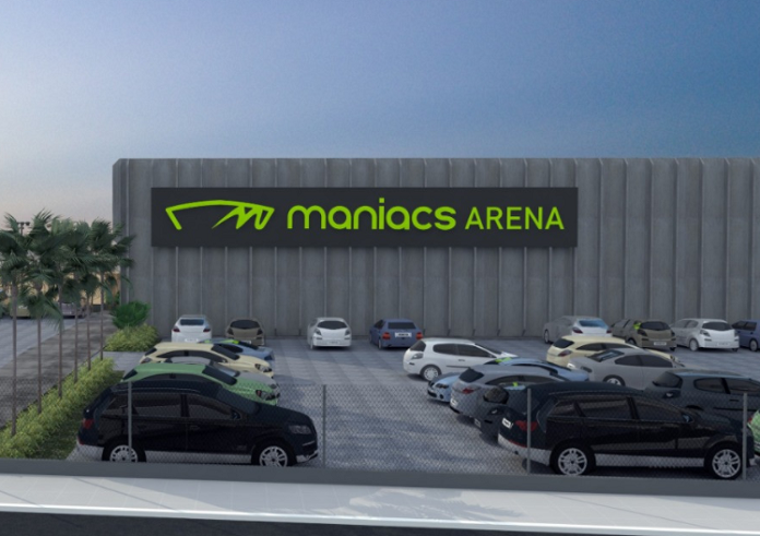 Projeto da arena de esportes de areia que será sediada em Biguaçu. Com um estacionamento e alguns carros, ao fundo se vê a arena identificada com letras verdes 