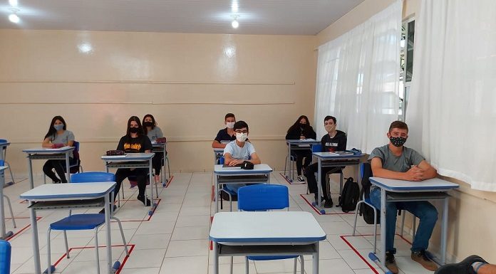 Alunos do ensino estadual de SC usam máscaras em sala de aula. É possível ver carteiras brancas com cadeiras azuis vazias.