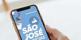 Uma mão segura um celular e o dedo indicador mexe na tela, que mostra a revista digital São José Notícias