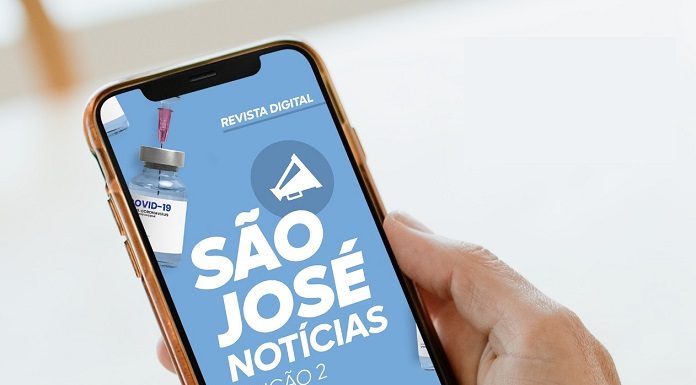 Uma mão segura um celular e o dedo indicador mexe na tela, que mostra a revista digital São José Notícias
