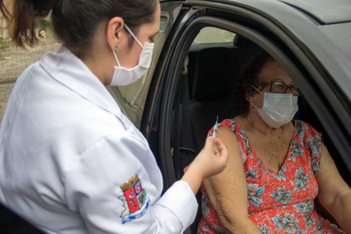 profissional de saúde com agulha na mão ao lado de senhora sentada em carro com a porta aberta