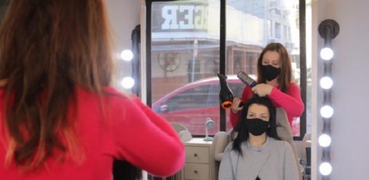Foto de um espelho, em que aparece uma mulher com secador mexendo no cabelo de uma moça que está sentada, ambas usam máscara. Os empreendedores de SC precisam lidar com o avanço da pandemia em meio a medidas restritivas e falta de amparo do governo.