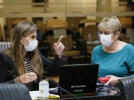 deputadas paulinha e luciane carminatti, de máscara, sentadas lado a lado na bancada da alesc, com computadores a frente; paulinha aponta para algo
