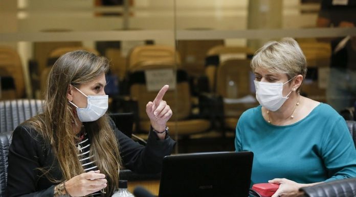 deputadas paulinha e luciane carminatti, de máscara, sentadas lado a lado na bancada da alesc, com computadores a frente; paulinha aponta para algo