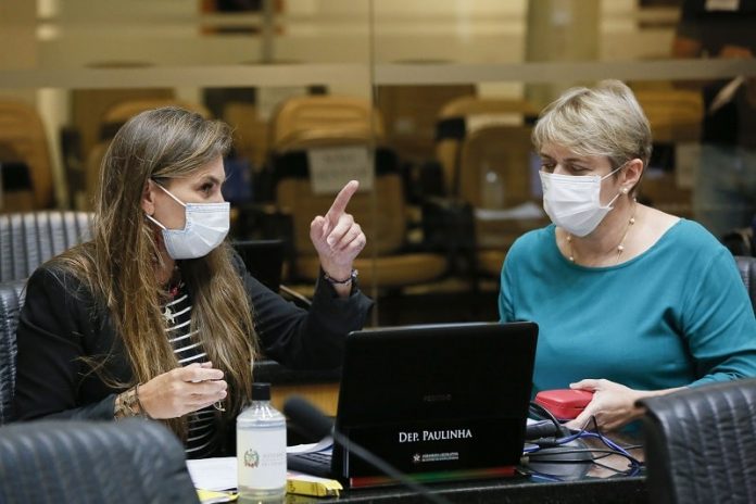 deputadas paulinha e luciane carminatti, de máscara, sentadas lado a lado na bancada da alesc, com computadores a frente; paulinha aponta para algo