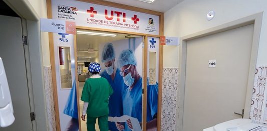 Hospitais da Grande Florianópolis seguem lotados, sem vagas em UTI para adultos ou crianças profissional de saúde com trajes de epi entra em porta de uti - Santa Catarina volta a quebrar recorde de mortes por Covid