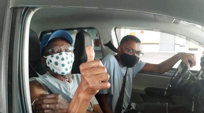 idoso faz sinal de joinha sentado no banco do carona e jovem motorista olha pra foto, ambos de máscara - quem pode se vacinar na grande florianópolis no fim de semana