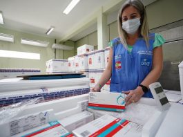 SC tem 2,1% da população vacinada, previsão de poucas doses em abril e mudança no lote funcionária usando máscara e colete confere caixas de doses de vacinas dentro de caixas de isopor