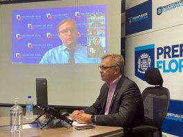 gean loureiro, presidente do consórcio conectar, em conversa online na prefeitura de florianópolis; outro homem projetado no telão ao fundo