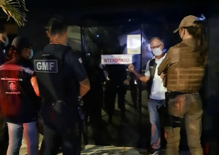 agentes de segurança em frente a um dos bares de florianópolis fiscailizados; porta de vidro fechada com placa 