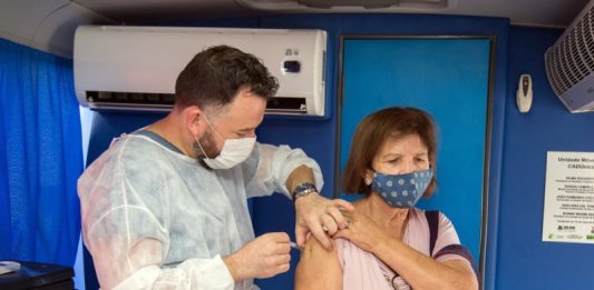idosa recebe vacina no braço aplicada por profissional usando epi dentro do ônibus de vacinação
