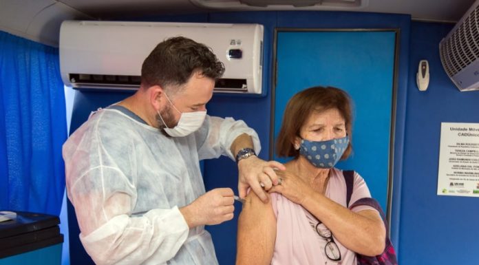 idosa recebe vacina no braço aplicada por profissional usando epi dentro do ônibus de vacinação