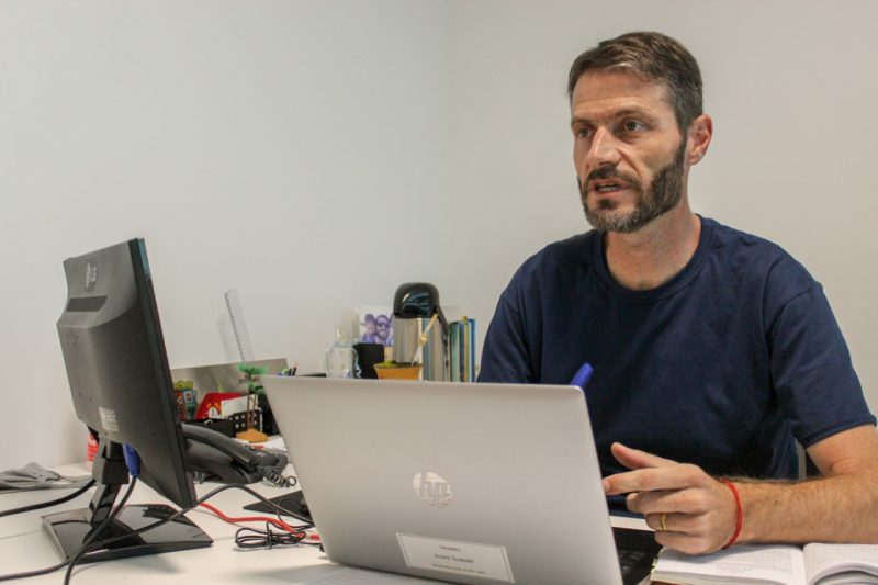 vereador andré guesser falando sentado em mesa com computador e notebook