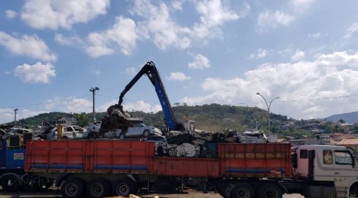 caminhão com braço mecânico recolhendo veículos sucateados em pilha