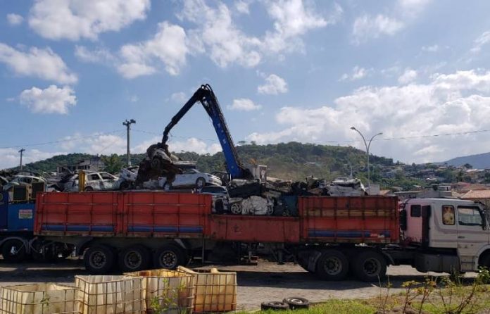 caminhão com braço mecânico recolhendo veículos sucateados em pilha