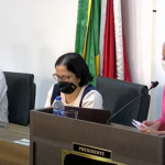 O vereador aparece de blusa blanca e máscara segurando o microfone, ele está sentado ao lado de uma mulher e mais ao lado está a presidente da câmara de são josé. No encontro, o secretario conversou com os vereadores sobre ações da pasta e a questão de pessoas em situação de rua na cidade.