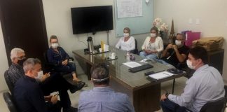 Em uma sala com uma mesa retangular ao centro, oito pessoas sentadas de forma circular conversam enquanto usam máscaras. Nessa reunião, entidades empresariais informaram a doação de recursos para obras do hospital regional de são josé.