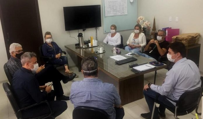 Em uma sala com uma mesa retangular ao centro, oito pessoas sentadas de forma circular conversam enquanto usam máscaras. Nessa reunião, entidades empresariais informaram a doação de recursos para obras do hospital regional de são josé.