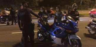 A foto em período noturno mostra uma moto parada com dois guardas municipais e duas pessoas conversando com eles, todo usam máscaras. Ao fundo uma movimentação de moto e carros. A GMF passa a utilizar um aparelho para identificas as motos em alta velocidade e emissão de ruídos