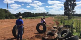Em uma estrada de terra, duas pessoas mexem em pneus que parecem abandonados. O programa do IMA visa o gerenciamento correto de resíduos, como os pneus.