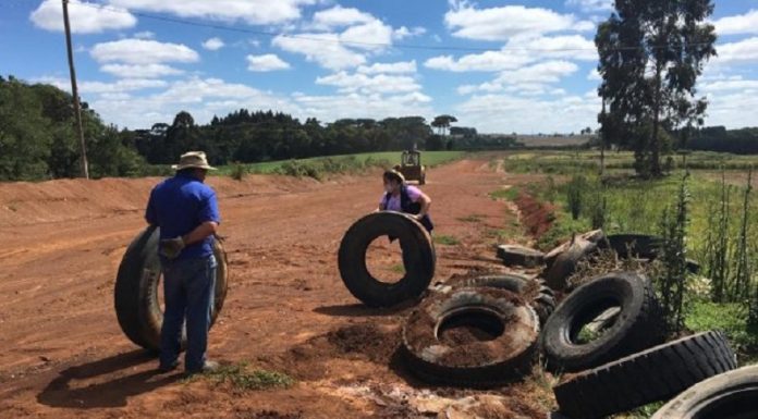 Em uma estrada de terra, duas pessoas mexem em pneus que parecem abandonados. O programa do IMA visa o gerenciamento correto de resíduos, como os pneus.