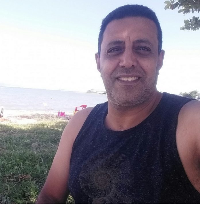 O motorista de aplicativo Amr Mostafa posa sorridente com uma regata preta, ele tem cabelos escuros e pele clara, Amr foi baleado em São José em uma corrida com três passageiros