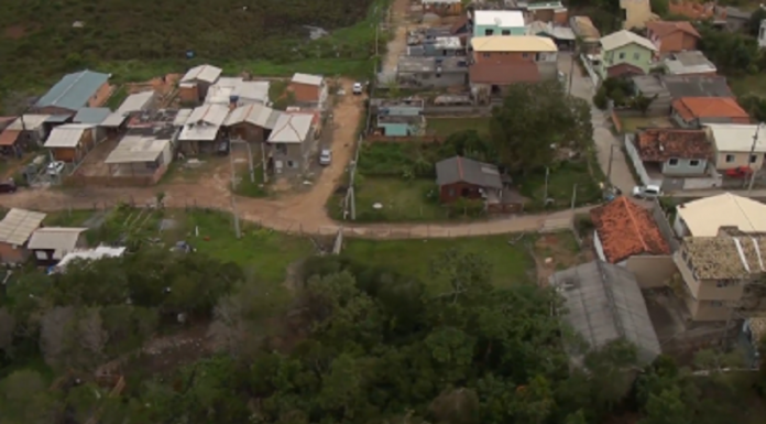 Vista aérea mostra área verde com ruas de terra e uma aparentemente asfaltada. Há diversas casas nessas ruas, representando as ocupações irregulares em Florianópolis, que descumpriu acordos em relação ao problema.