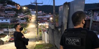 dois policiais civis olham para residência em ladeira com muitas casas ao fundo no início da 3ª fase da operação héracles